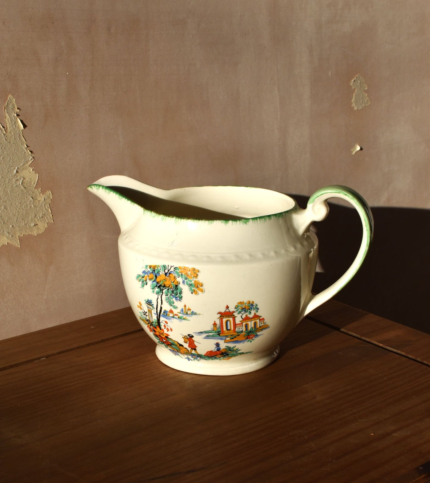 Decorative ceramic pitcher with floral and landscape design on a wooden surface.