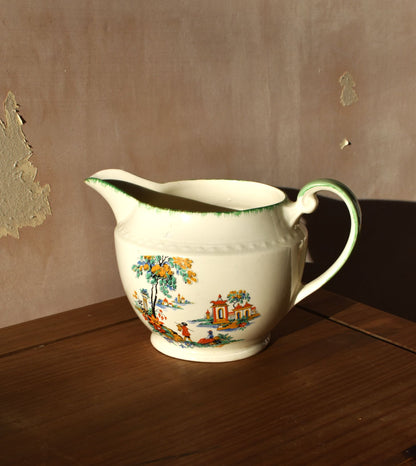 Decorative ceramic pitcher with floral and landscape design on a wooden surface.