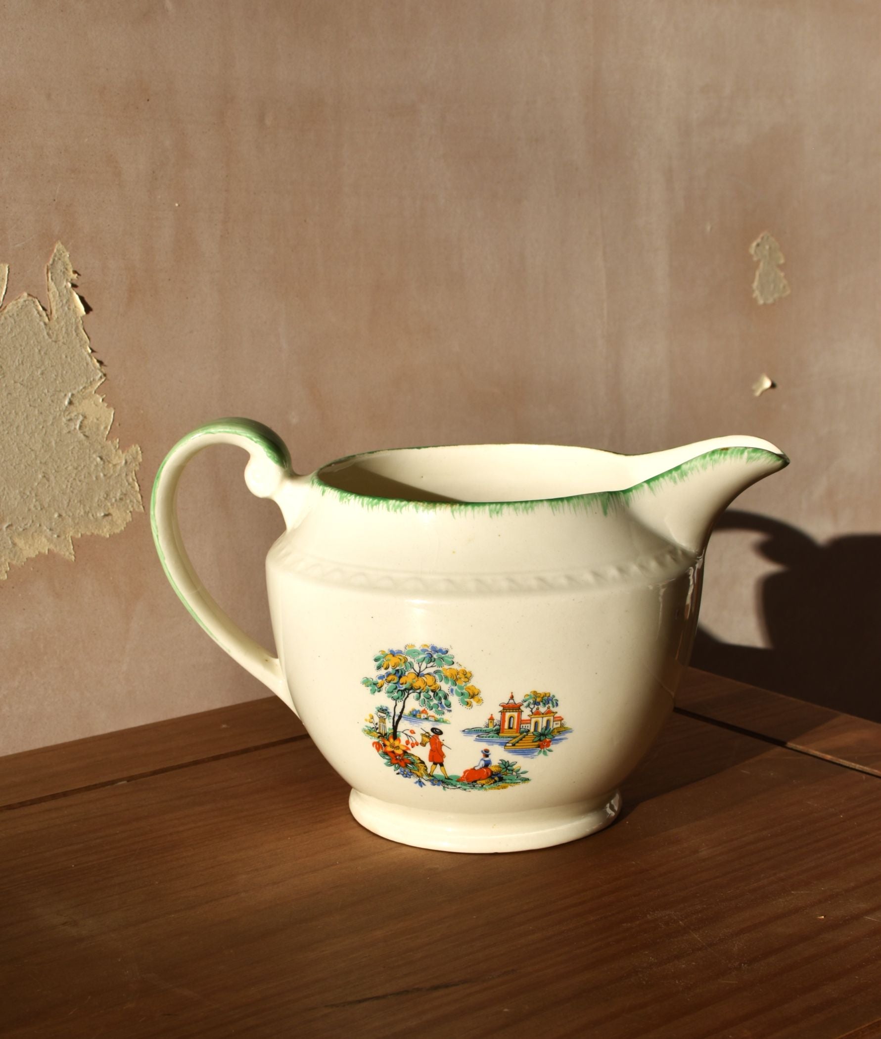 Vintage-style ceramic pitcher with decorative design on a wooden surface.