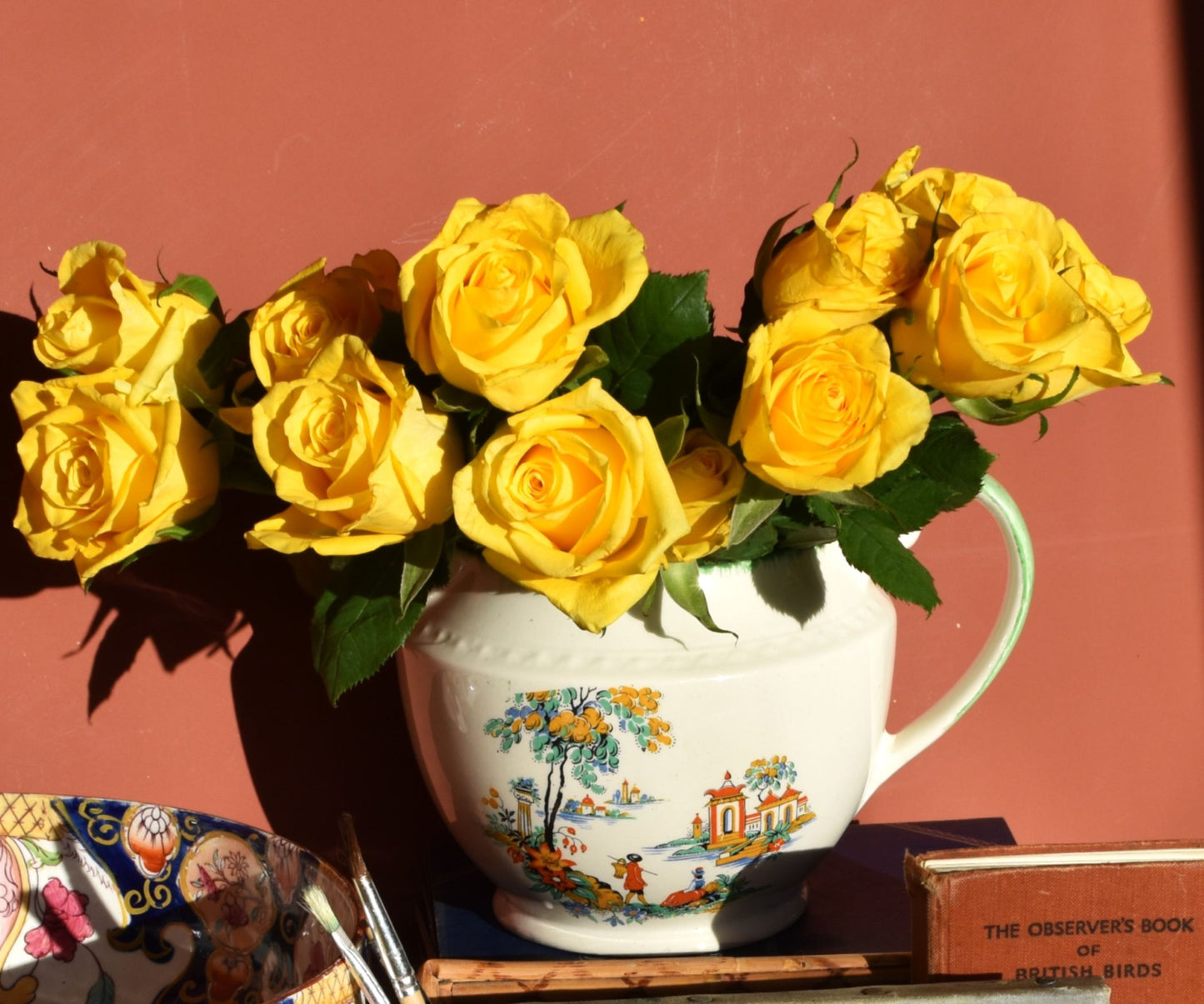 Bouquet of yellow roses in a decorative jugagainst a red background