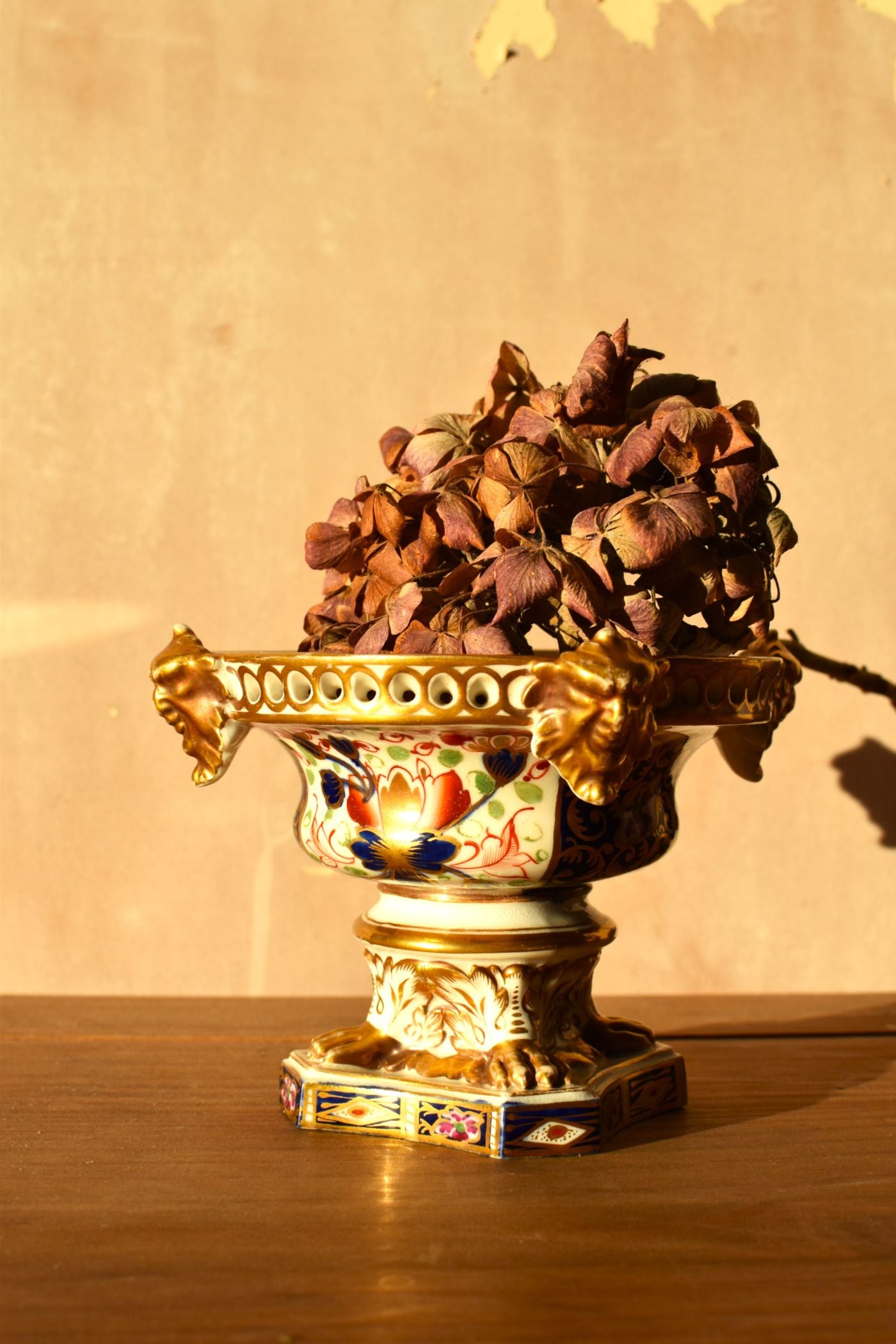 Decorative urn with gold detailing and dried flowers on a wooden surface.