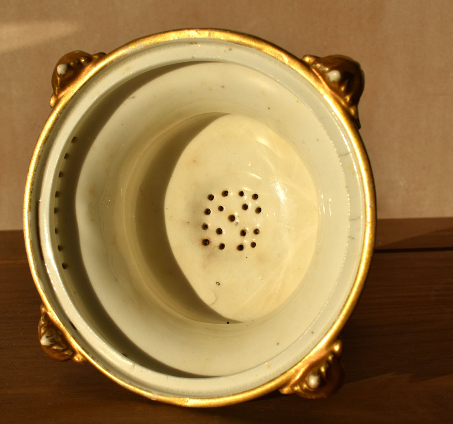 Decorative ceramic strainer with gold rim on a wooden surface