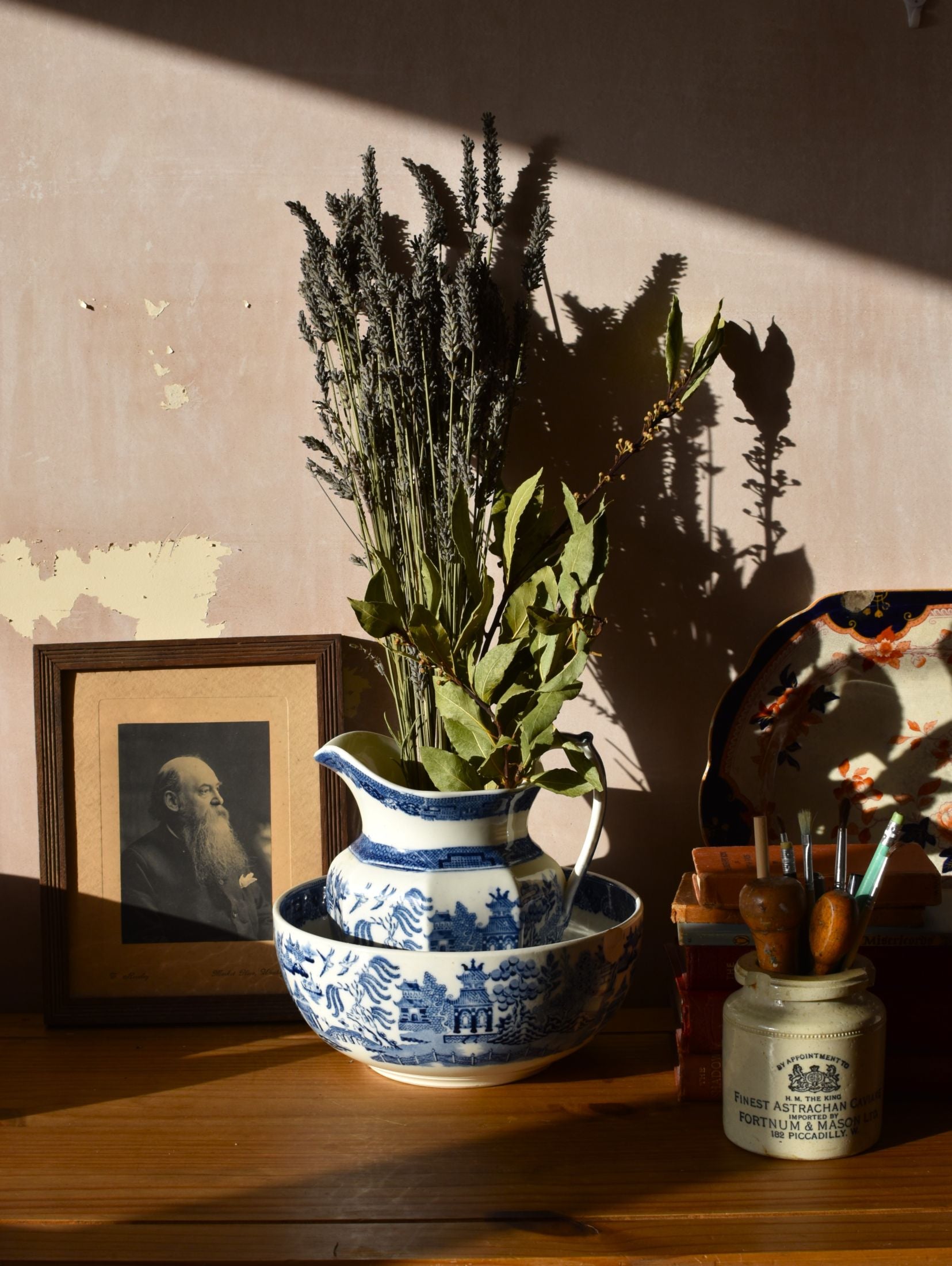 Decorative still life with a blue and white pitcher, bowl, and dried plants on a wooden surface.