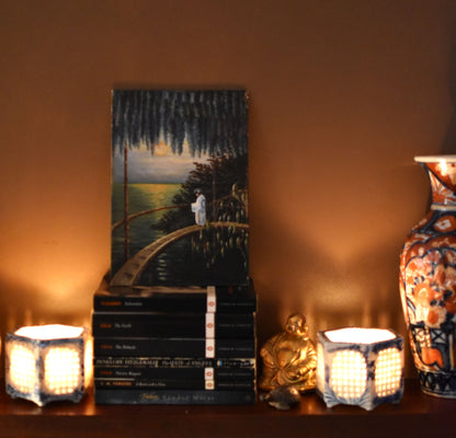 Decorative setup with an oil painting, books, a vase, and candles on a table against a warm background